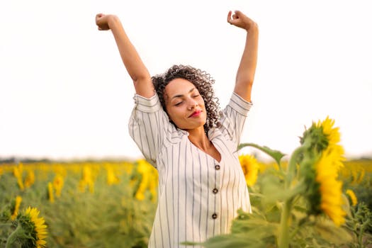 A woman stretches in a vibrant sunflower field, enjoying the sunny outdoors and simple happiness.