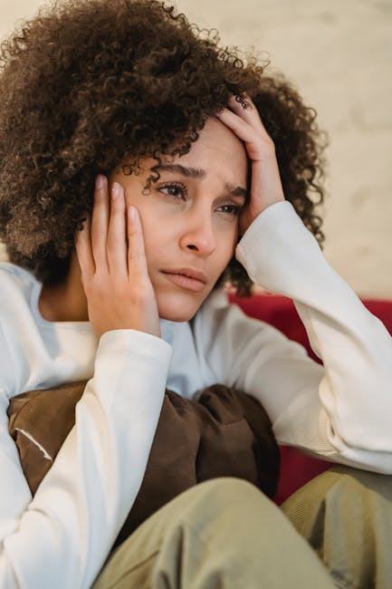 A woman indoors sitting with a pillow and contemplating deeply, reflecting emotions.