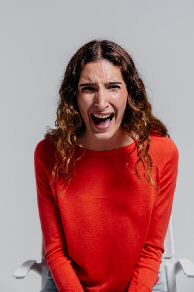 A woman in a red sweater shouting, displaying anger and emotion.